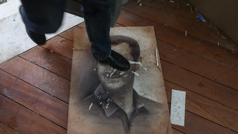 A man treads on a picture of Syria's ousted president Bashar al-Assad as people enter his residence in Damascus' Malki area
