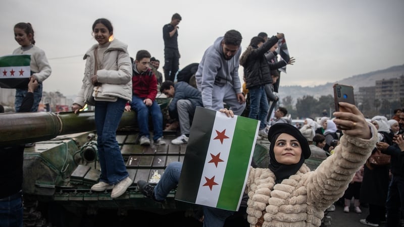 A woman takes a selfie in front of a destroyed tank in Umayyad Square, Damascus