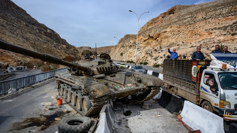 People drive past an abandoned Syrian army tank near the Lebanon border