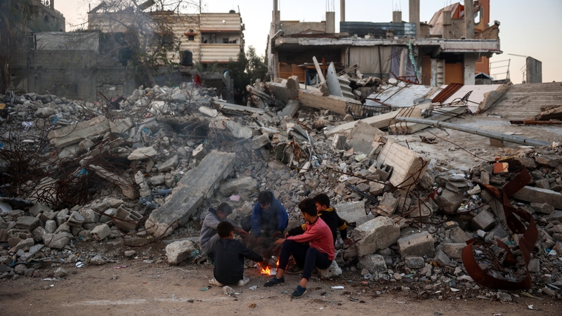 Children warm by a fire next to the rubble of destroyed buildings at Bureij refugee camp