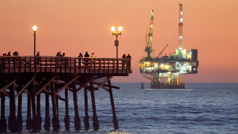 People are seen on a pier with offshore oil and gas platform Esther in the distance in Seal Beach, California