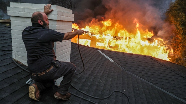 A man shields from intense heat as he hoses down a neighbour's rooftop on Sinaloa Ave in Atadena as the Eaton Fire continues to grow