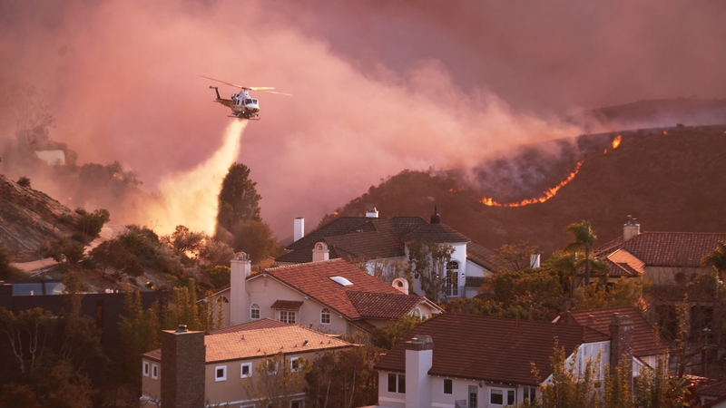 A helicopter drops water around homes threatened by the Palisades Fire in California