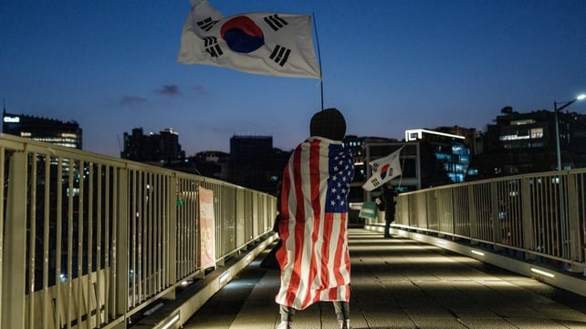 A supporter of impeached South Korean President Yoon Suk Yeol waves a South Korean flag as she wears a US flag on a pedestrian bridge near the president's residence in Seoul