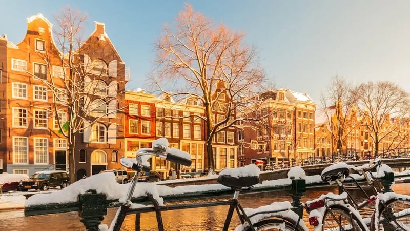 Bicycles covered with snow alongside a canal during winter in Amsterdam (Alamy/PA)