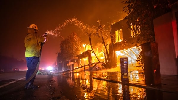 A firefighter battles the Palisades Fire while it burns homes