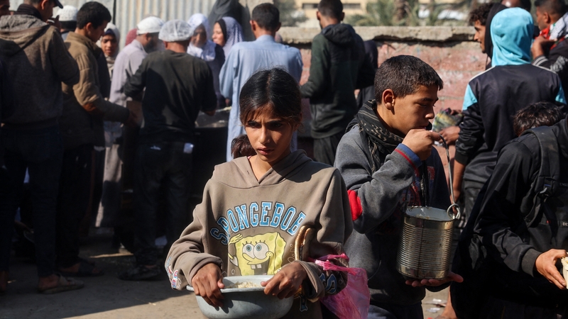 Palestinian children receive aid food being distributed in the Deir al-Balah in central Gaza following the announcement of a truce