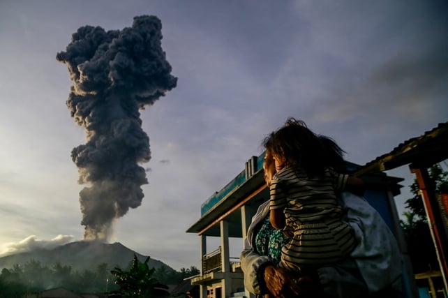 A woman and child look on as volcanic ash rises into the air during the eruption of Mount Ibu, Indonesia