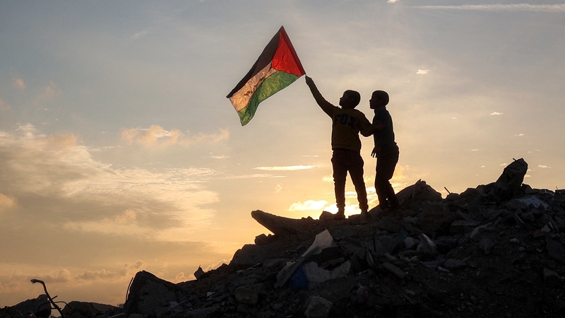 A boy runs with a Palestinian flag atop a mound of rubble at a camp for displaced people in central Gaza