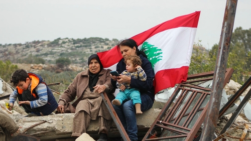Displaced residents lift a Lebanese flag as they sit on the rubble of their home in their southern Lebanese village of Yarin