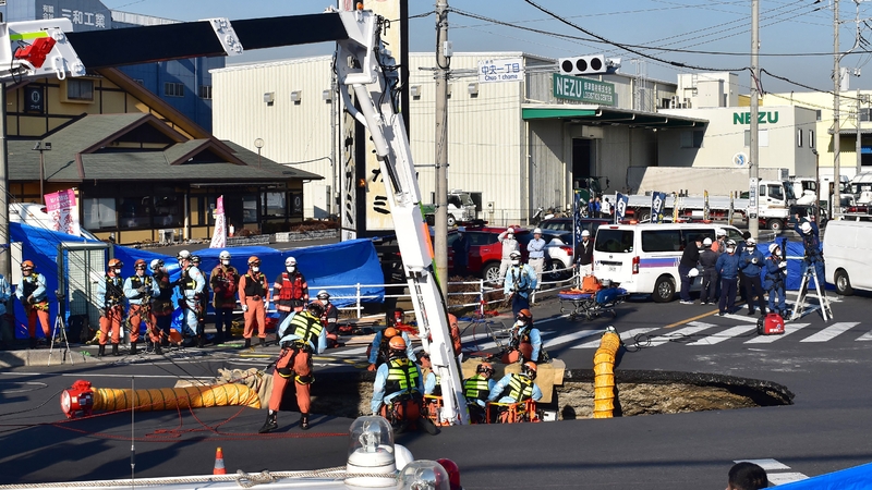 Firefighters work to rescue the truck driver from the sinkhole on a road in Yashio