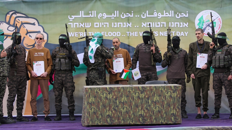 Palestinian Hamas fighters escort the three Israeli hostages on a stage before handing them over to a Red Cross team