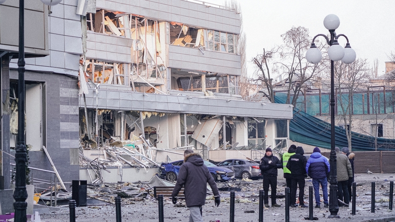 People and police officers stand in the background of a damaged building after a Russian missile attack in Kyiv