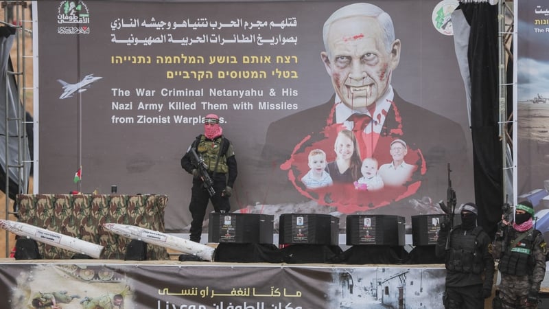Armed Hamas members stand on a stage next to four black coffins before handing them over to the Red Cross