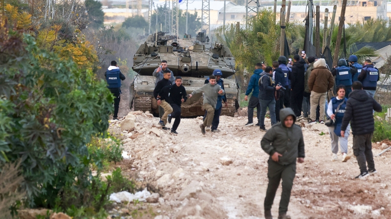 Iriseoirí agus daoine eile os comhair tanc de chuid Arm Iosrael ar an mbóthar go Jenin