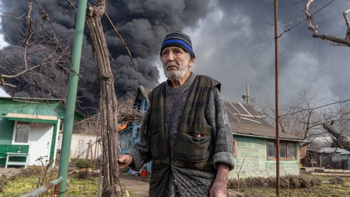 A man stands in the courtyard of his house while smoke rises from a fire following a strike on the outskirts of Odessa earlier this week