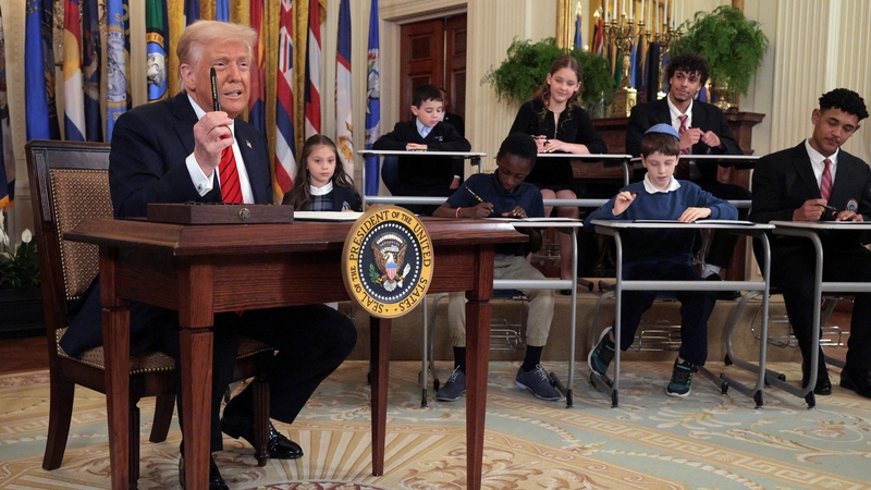 President Trump signs the executive order alongside school children signing their own versions