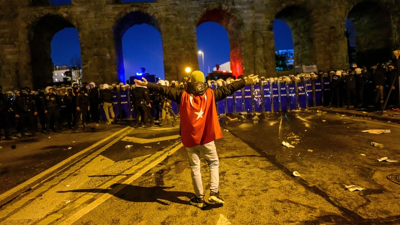 A protesters wearing a Turkish flag gestures in front of riot police standing in a blocking formation at a demonstration