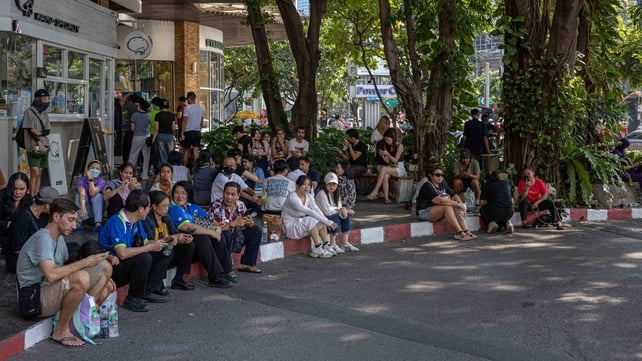 People wait outside after fleeing buildings in Bangkok