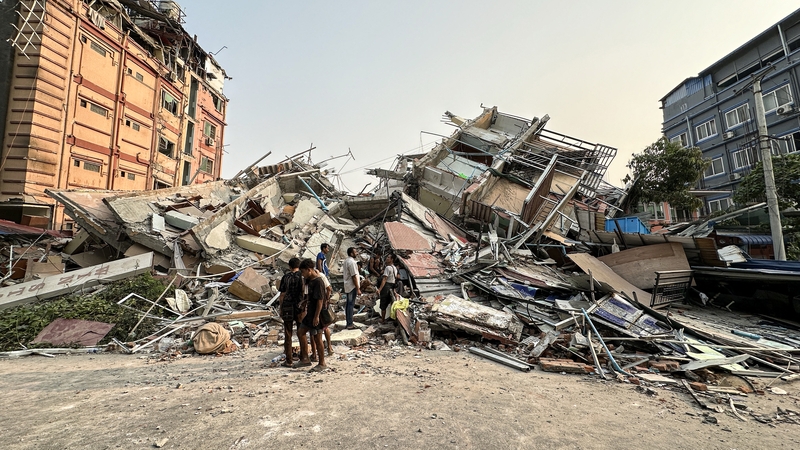 People stand near the debris of a collapsed building in Myanmar