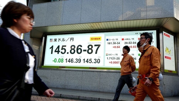 People walk past an electronic board showing the foreign exchange trading price of the Japanese yen against the US dollar on a street in Tokyo