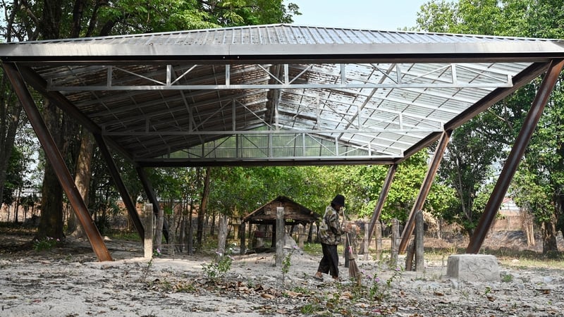 A woman sweeps beneath the clear plastic roof over the cremation site of Pol Pot in Anlong Veng