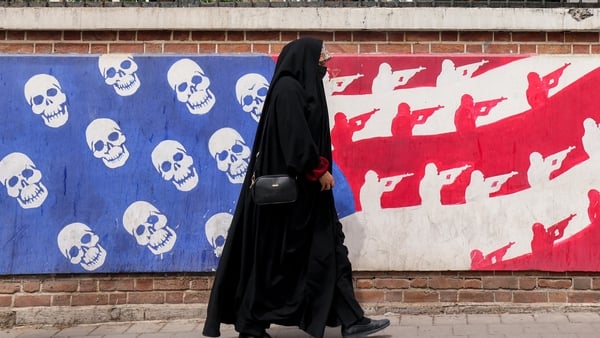 A woman walks past a mural depicting the US flag substituted with skulls and soldiers, painted on the outer walls of the former US embassy in Tehran