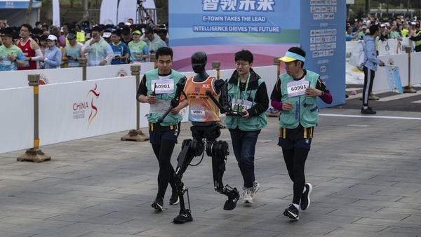 A humanoid robot called Tiangong runs with support technicians in the Beijing E-Town Humanoid Robot Half Marathon