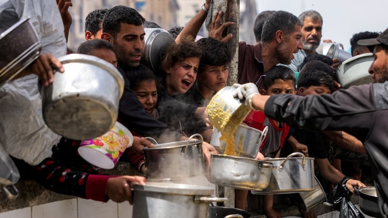 People queue with pots to receive charity meals from an aid kitchen in Beit Lahia in northern Gaza