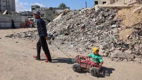 A Palestinian man pulls a child sitting in a makeshift cart along a road next to a destroyed building in Gaza city