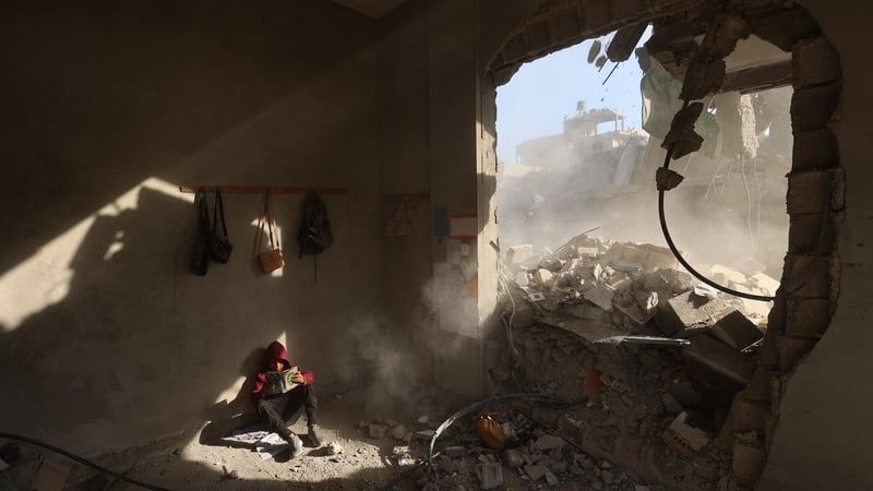 A Palestinian boy holds a book as he sits in rubble of a house, following overnight Israeli strikes at the Nuseirat refugee camp