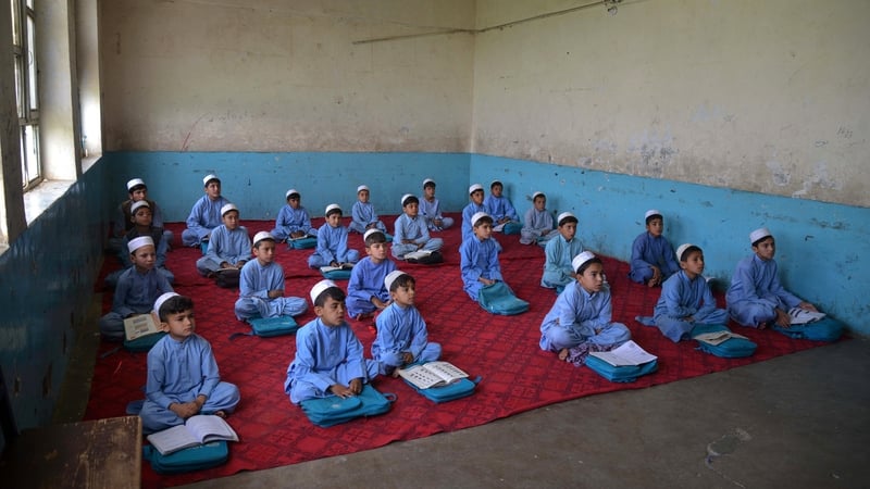 Afghan schoolboys, wearing salwar kameez and white hats as part of a new uniform code, attend class at a school in Kandahar