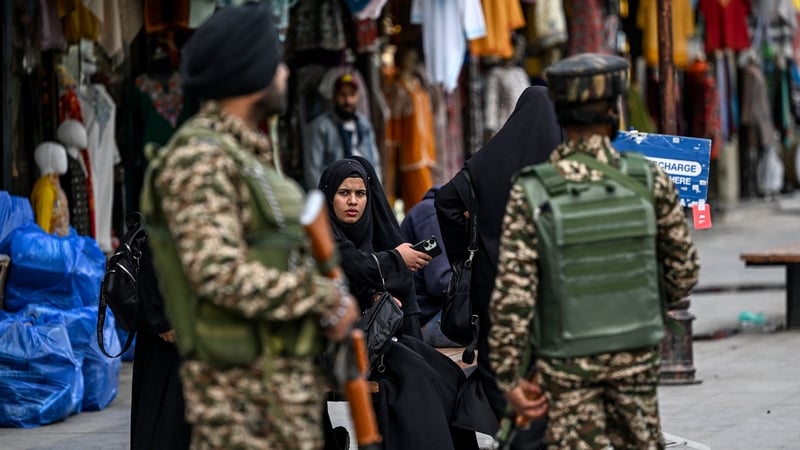 Kashmiri women sit on a bench at a marketplace as Indian paramilitary soldiers stand guard in Srinagar
