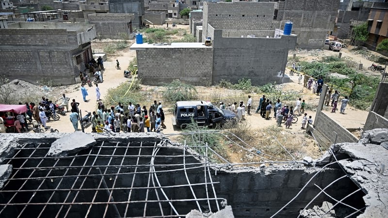 Residents gather as police personnel inspect the site where an alleged drone was shot down in Karachi