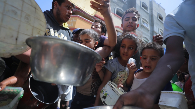 Palestinians in Gaza wait in queues to receive pots of food distributed by a charity organisation