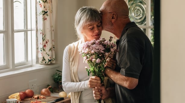 Senior couple standing in kitchen holding a bunch of flowers