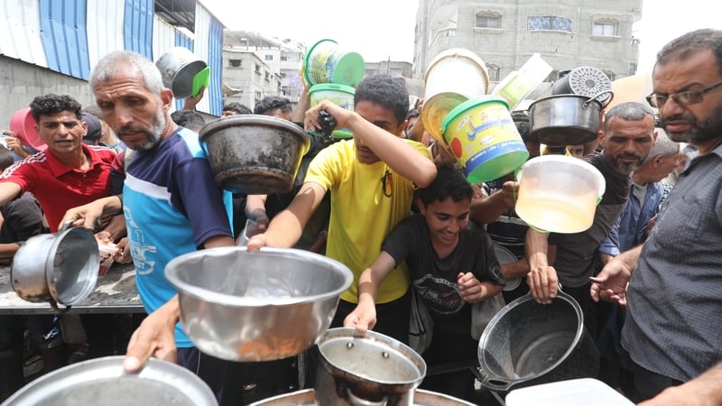 Palestinians wait in line to receive hot meals distributed by a charity