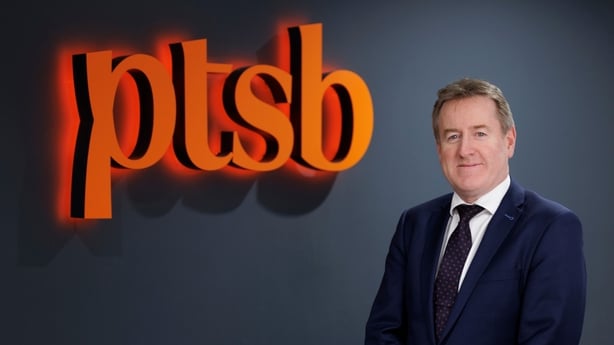 Eamonn Crowley, the CEO of PTSB beside an orange logo of the bank