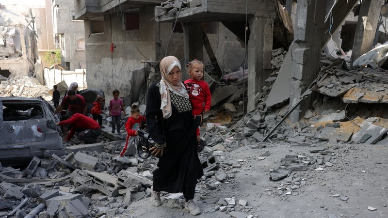 A Palestinian woman carries a toddler as she walks amid the destruction following Israeli strikes in Jabalia's Saftawi neighbourhood