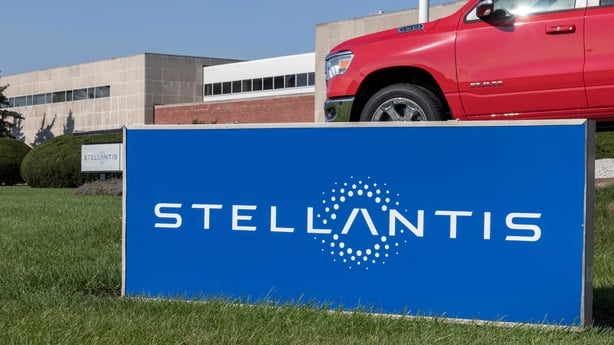 a blue sign with white text and the Stellantis logo in front of a red vehicle parked in front of a building