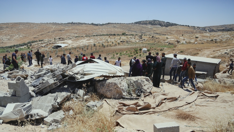 Palestinians walk past the remains of houses demolished by Israeli forces south of Hebron, West Bank