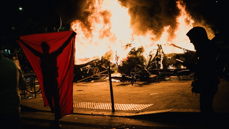 A person with a flag seen in front of two cars on fire during celebrations near the Parc des Princes stadium