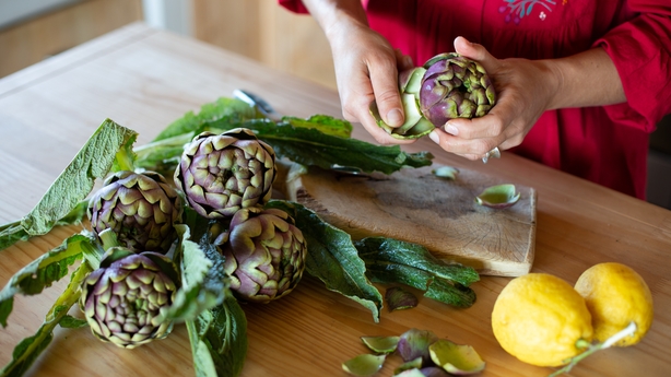 a person holding artichokes on a table