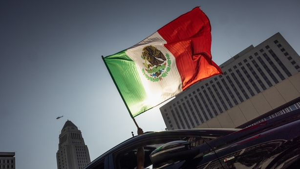 LOS ANGELES, CALIFORNIA - JUNE 8: A car is seen waving a flag of Mexico out of their sunroof, while driving down Los Angeles Street as demonstrators protest immigration raids and the presence of National Guard Troops on June 8, 2025 in downtown Los Angeles, California. Los Angeles has seen protests