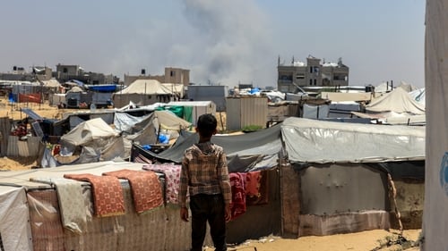 A Palestinian child looks on as smoke billows in the distance during Israeli bombardment in Rafah