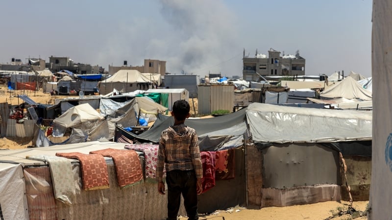 A Palestinian child looks on as smoke billows in the distance during Israeli bombardment in Rafah