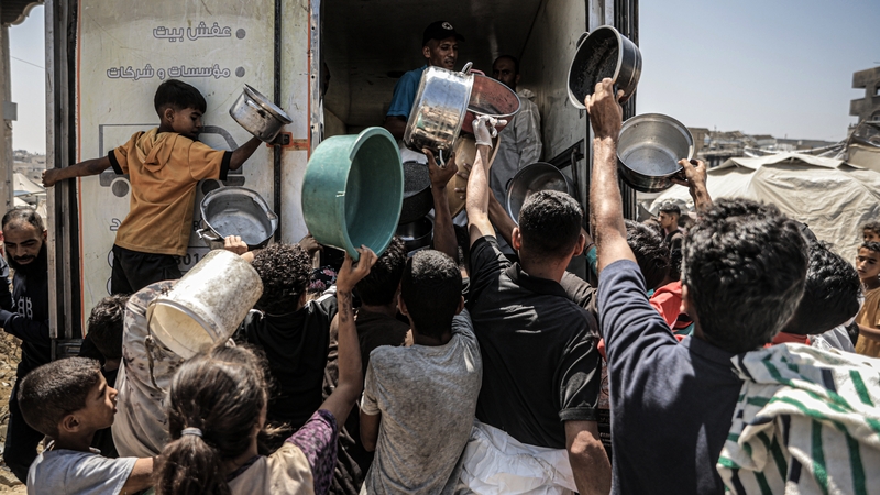 Displaced Palestinians gather to receive hot meals distributed by a charity organisation at Sheikh Radwan