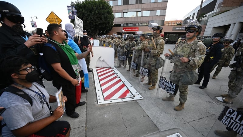 Protestors stand and kneel in front of a row of California National Guard members in Los Angeles