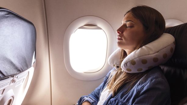 A young woman rests her head on a neck pillow and sleeps on the flight