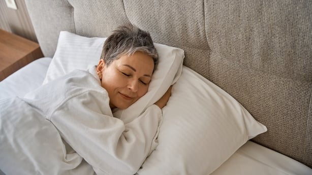 Adult lady in white bathrobe resting in hotel room while sleeping on cozy pillow. Travel, people, lifestyle concept